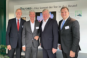 A group photo of four men in suits, standing side by side and smiling. Seen (from left to right): Michael Spethmann, Jörg A. Gerdes, Dr. Bernd Althusmann and Lars Wagener. They are standing in front of an Milford advertising wall.
