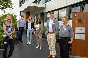 A photo of the trainees from the year 2020. Six people, including four women and two men, are wearing business attire and standing in front of the entrance to the OTG location in Hittfeld, Seevetal. 