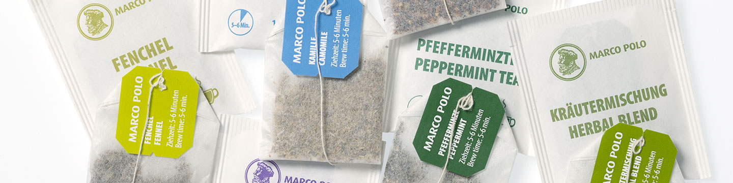 Teebeutel und die Verpackungen von diesen Beuteln liegen verteilt auf dem Tisch. Sie sind von der Teemarke Marco Polo.